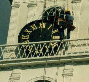 A historic reproduction of a clock face is hoisted into position with newly gilded roman numerals.